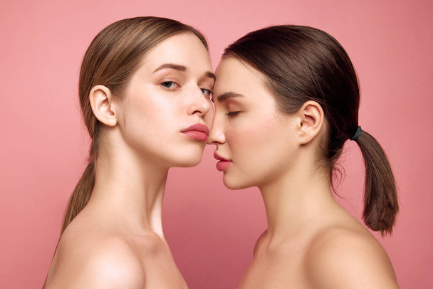 Unfiltered charm. Girls embrace natural beauty as one. Close up of two pretty ladies with bare shoulders posing against pink studio background. Concept of health, self care, cosmetic products, make-up - Photo, Image
