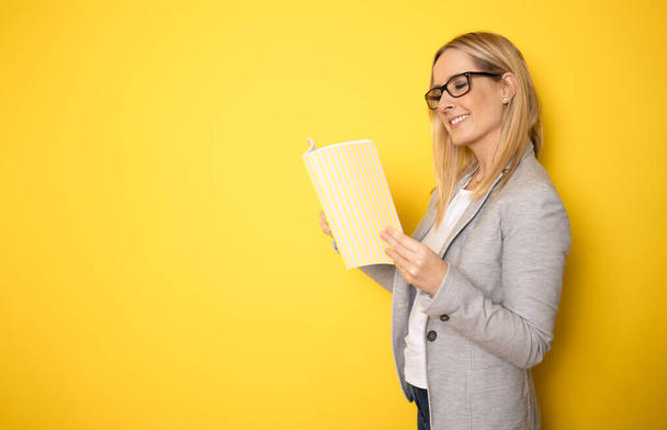 Souriante enseignante ou femme d'affaires tenant un livre jaune portrait isolé. - Photo, image