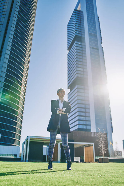 obecný záběr mladé asijské podnikatelky v moderním obleku s bílými vlasy zkřížené ruce s mrakodrapy v pozadí a zadní světlo - Fotografie, Obrázek