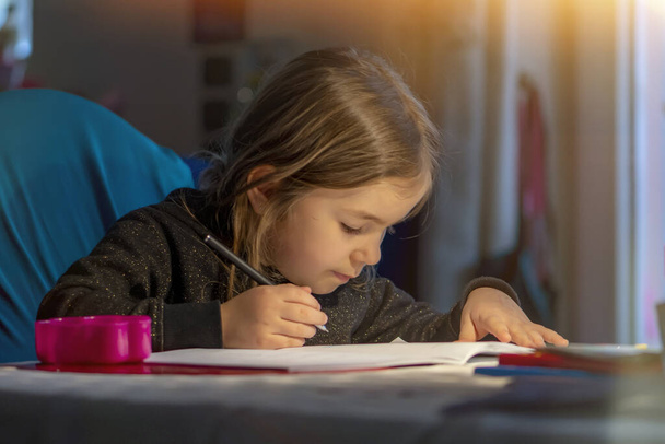 Egy szőke hajú lány portréja, aki esténként egy asztali lámpa fényében tanul.. - Fotó, kép