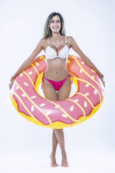 Vrouw in bikini met grote opblaasbare zwemring over een grijze achtergrond. - Foto, afbeelding