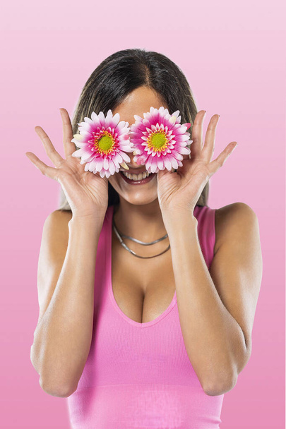 Nuori nainen peittää silmät kukkia vaaleanpunainen paita vaaleanpunainen tausta. - Valokuva, kuva