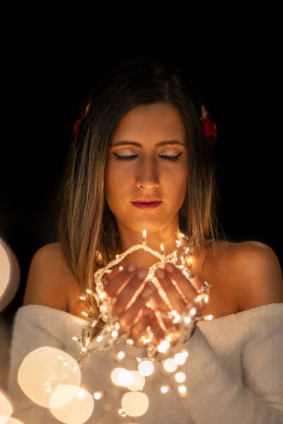 異なるポーズで黒い背景の上にクリスマスの弦ライトを保持している若い女性. - 写真・画像