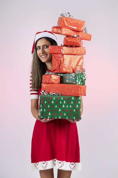 Weiblicher Weihnachtsmann hält Stapel von Geschenken über rotem Hintergrund. - Foto, Bild