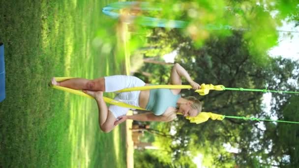Mujer adulta practica aero yoga en hamaca en parque. Ejercicio deportivo meditación zen entrenamiento al aire libre. Estiramiento femenino para la flexibilidad del cuerpo de salud. aliviar el estrés para el bienestar físico y emocional - Metraje, vídeo
