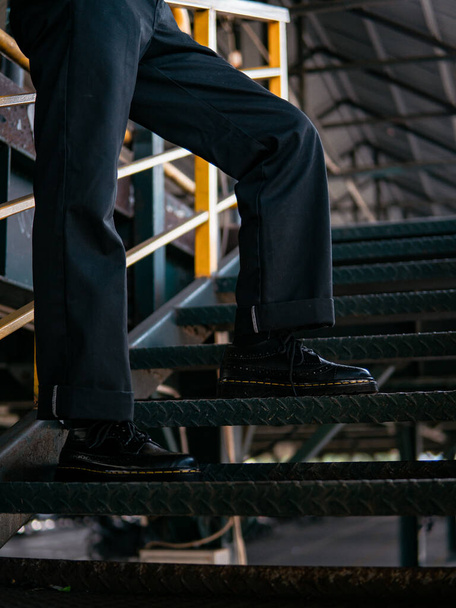 Close-up van de volledige zwarte vleugeltip brogue schoenen gemaakt van echt leer gedragen door een mannelijk model in een verlaten magazijn. Onderwerp foto van klassieke vleugeltip brogue schoenen in een oud gebouw gemaakt van ijzer - Foto, afbeelding