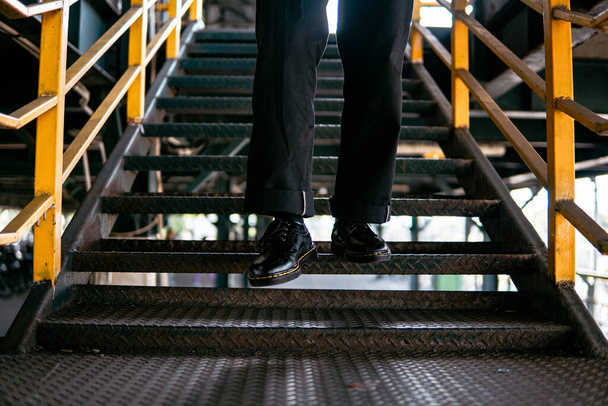 Terk edilmiş bir depoda erkek bir mankenin giydiği hakiki deriden yapılmış siyah kanat uçlu ayakkabıların yakın görüntüsü. Demirden yapılmış eski bir binada klasik kanat ucu ayakkabı konsepti. - Fotoğraf, Görsel