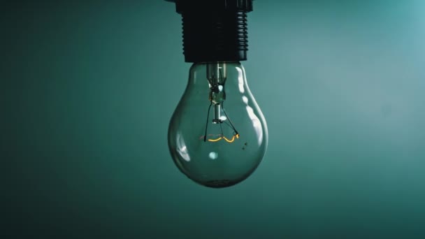 Light bulb flashes on a blue background in the dark. Slow turning on and off of a tungsten light bulb. Filament of a blinking vintage light bulb. Energy, electricity, light, life. - Video, Çekim