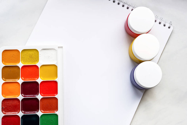 Bunte Aquarell- oder Acrylfarben und Bleistifte auf einem weißen Blatt Papier auf weißem Hintergrund. Design Studio Tischplatte Ansicht. Raum für Text. - Foto, Bild