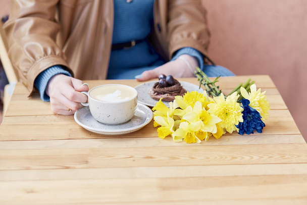 Pausa caffè accogliente - donna che si gode il latte e il dessert al cioccolato con narcisi primaverili. - Foto, immagini
