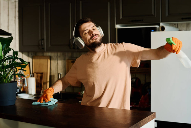 Nuori mies kuulokkeet nauttia aurinkoinen päivä ja hänen suosikki musiikkia seistessään keittiössä laskuri ja suorittaa kotitöitä - Valokuva, kuva