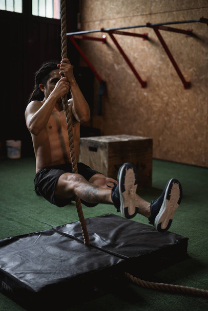 man in de sportschool doet klimtouw - Foto, afbeelding