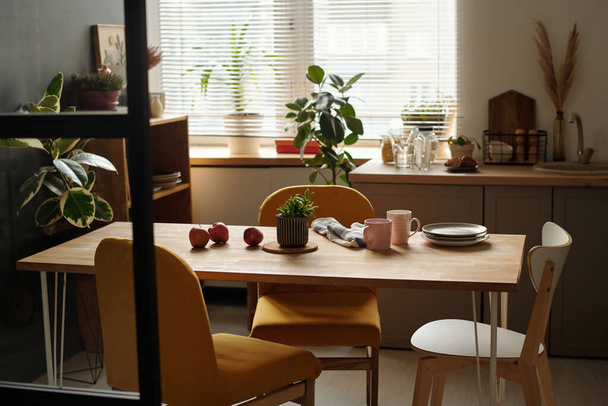 Ahşap masanın etrafında duran sandalyeler yeşil yerli bitkilerle, taze elmalarla ve mutfak malzemeleriyle. - Fotoğraf, Görsel