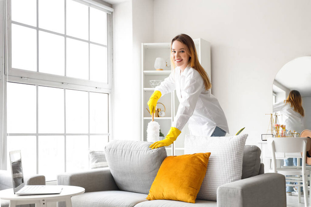 Mujer joven limpiando sofá con pp-duster en casa - Foto, imagen
