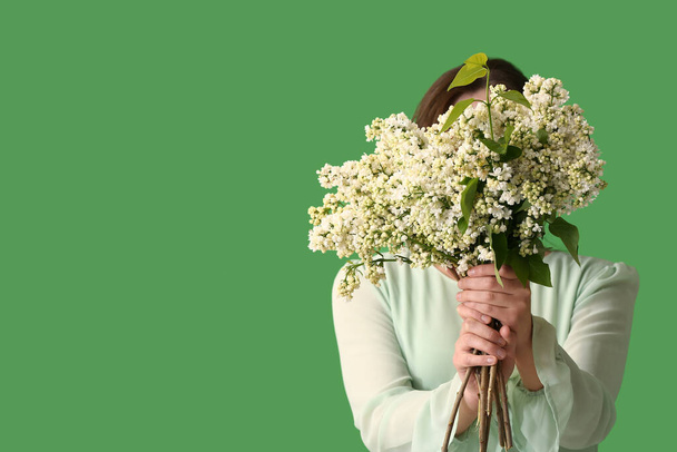Young woman with bouquet of lilac flowers on green background - Photo, Image
