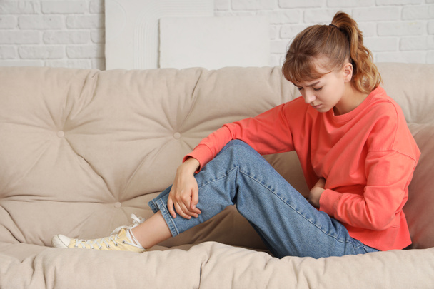 Молодая женщина страдает от боли в животе на диване дома - Фото, изображение