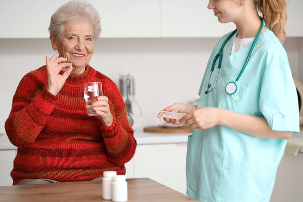 Idősebb nő orvossal tablettát szed a konyhában - Fotó, kép
