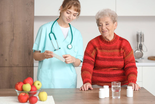 キッチンでシニア女性に錠剤ボトルを示す医師 - 写真・画像