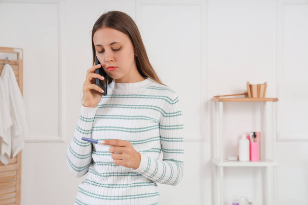 Young lesbian woman with pregnancy test talking by mobile phone in bathroom - Photo, Image