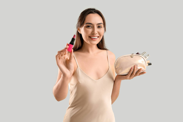 Kaunis nuori nainen meikkilaukku täynnä meikkituotteita ja huulipunaa harmaalla taustalla - Valokuva, kuva