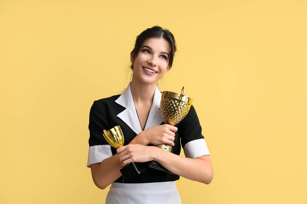 Camarera joven con copas de oro sobre fondo amarillo - Foto, imagen