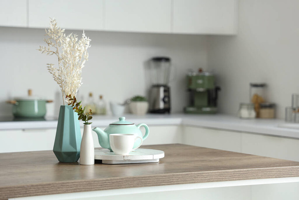 Houten tafel met theeset, gedroogde bloemen en eucalyptustakken in moderne keuken - Foto, afbeelding