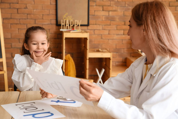 Petite fille mignonne avec orthophoniste prononçant des lettres à la table au bureau - Photo, image