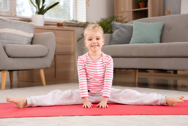 Симпатична маленька дівчинка практикує йогу на килимку у вітальні - Фото, зображення