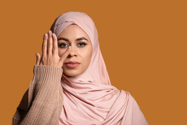 Joven mujer musulmana afroamericana con hermoso maquillaje sobre fondo marrón - Foto, imagen