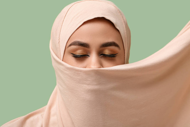 Pretty young African-American Muslim woman with beautiful makeup on green background - Photo, Image