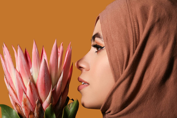 Jonge Afro-Amerikaanse moslim vrouw met mooie make-up en bloem op bruine achtergrond - Foto, afbeelding