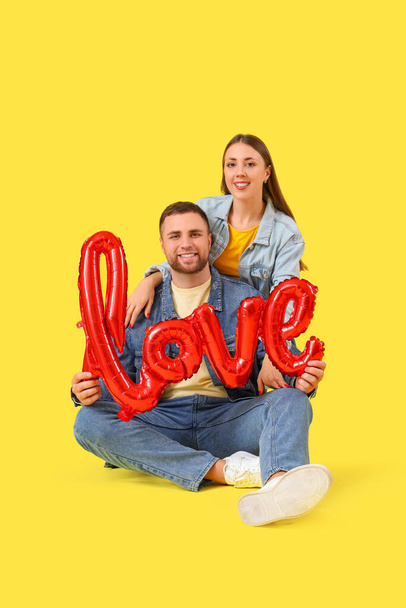 Krásný pár se slovem LOVE vyrobený z balónků na žlutém pozadí. Valentýnská oslava - Fotografie, Obrázek