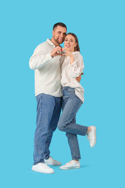 Preciosa pareja haciendo corazón con sus manos sobre fondo azul. Celebración de San Valentín - Foto, imagen
