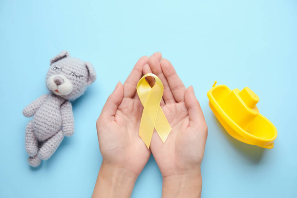 Female hands with golden awareness ribbon and toys on blue background. International Childhood Cancer Day - Photo, Image
