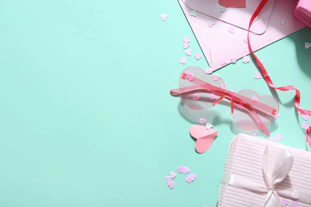 Розовые очки в форме сердца с конвертом, подарком и декором на бирюзовом фоне. День святого Валентина - Фото, изображение