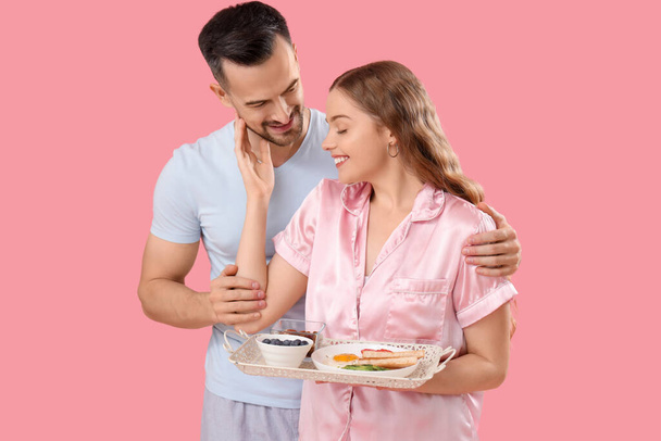 Νεαρό ζευγάρι με νόστιμο πρωινό σε ροζ φόντο. Γιορτή του Αγίου Βαλεντίνου - Φωτογραφία, εικόνα