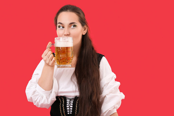 Молодая ирландка с кружкой пива на красном фоне. Празднование Дня Святого Патрика - Фото, изображение