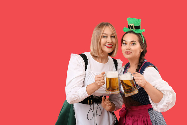Mujeres felices con cerveza celebrando el Día de San Patricio sobre fondo rojo - Foto, imagen