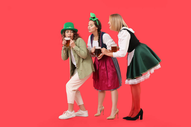Portrait of women with beer celebrating St. Patrick's Day on red background - Photo, Image