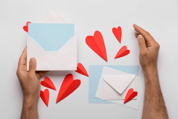 Manos masculinas con sobres, tarjetas en blanco y corazones de papel rojo sobre fondo blanco. Celebración de San Valentín - Foto, Imagen