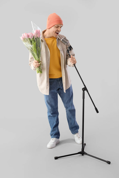 Artista masculino con tulipanes cantando sobre fondo claro. Celebración del Día Internacional de la Mujer - Foto, imagen
