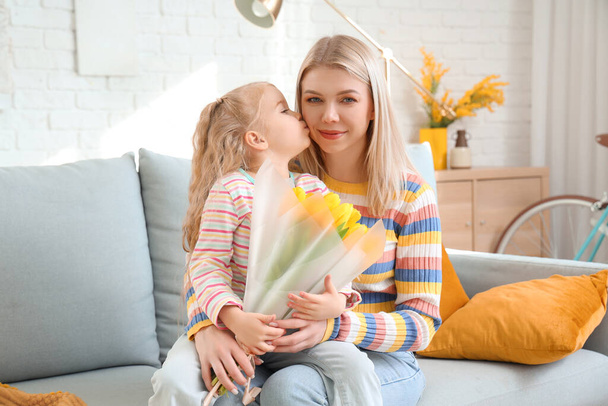 Маленька дівчинка з тюльпанами цілує маму на дивані вдома. Міжнародний жіночий день - Фото, зображення