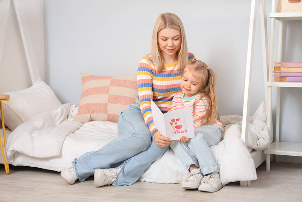 Klein meisje en haar moeder met wenskaart in de slaapkamer. Internationale Vrouwendag viering - Foto, afbeelding