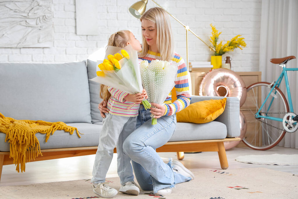 Petite fille avec des tulipes et sa mère assise sur le canapé à la maison. Célébration de la Journée internationale de la femme - Photo, image