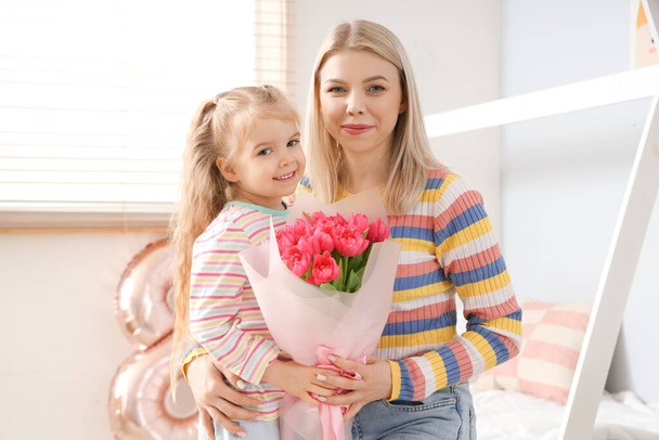 Niña con tulipanes y su madre en el dormitorio. Celebración del Día Internacional de la Mujer - Foto, imagen