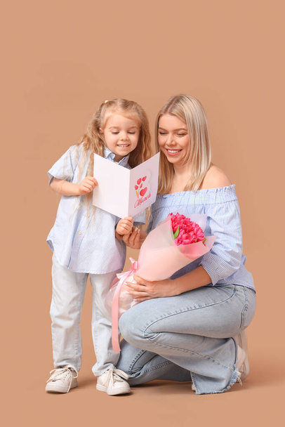 Niña con tarjeta de felicitación y su madre sobre fondo beige. Celebración del Día Internacional de la Mujer - Foto, imagen
