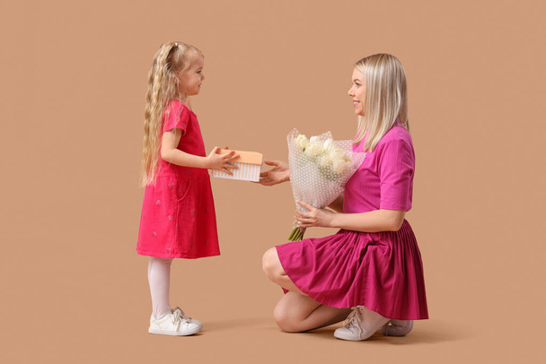 Klein meisje begroet haar moeder met geschenk op beige achtergrond. Internationale Vrouwendag viering - Foto, afbeelding