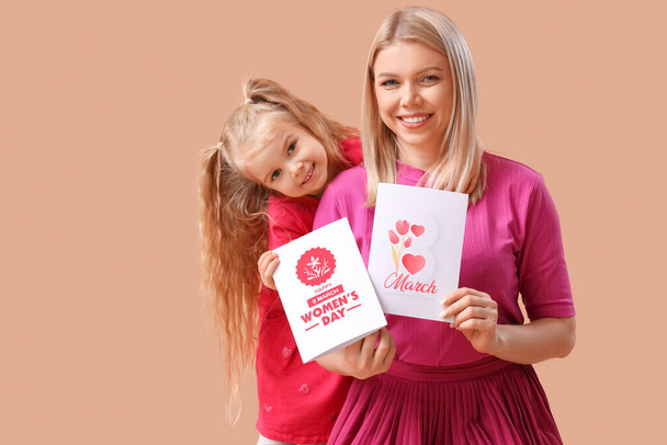 Kleines Mädchen und ihre Mutter mit Grußkarten auf beigem Hintergrund. Feier zum Internationalen Frauentag - Foto, Bild