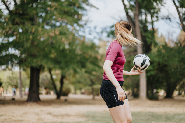 Uma mulher atraente gosta de atividades de fitness ao ar livre, mostrando suas habilidades de futebol livre e malabarismo com uma bola de futebol. - Foto, Imagem