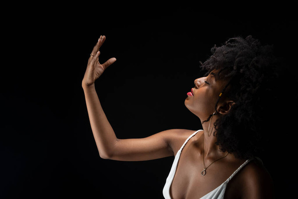 Beautiful woman, with black power hair, making movements with her arms. Wearing white clothes. Isolated on black background. - Foto, afbeelding